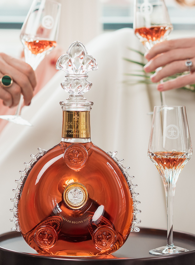 A lifestyle photo of an engraved decanter with a crystal glass aside. Two hands with crystal glasses in the background.