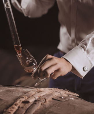 A photo of a person serving cognac to a glas using glass spear, barrel beneath