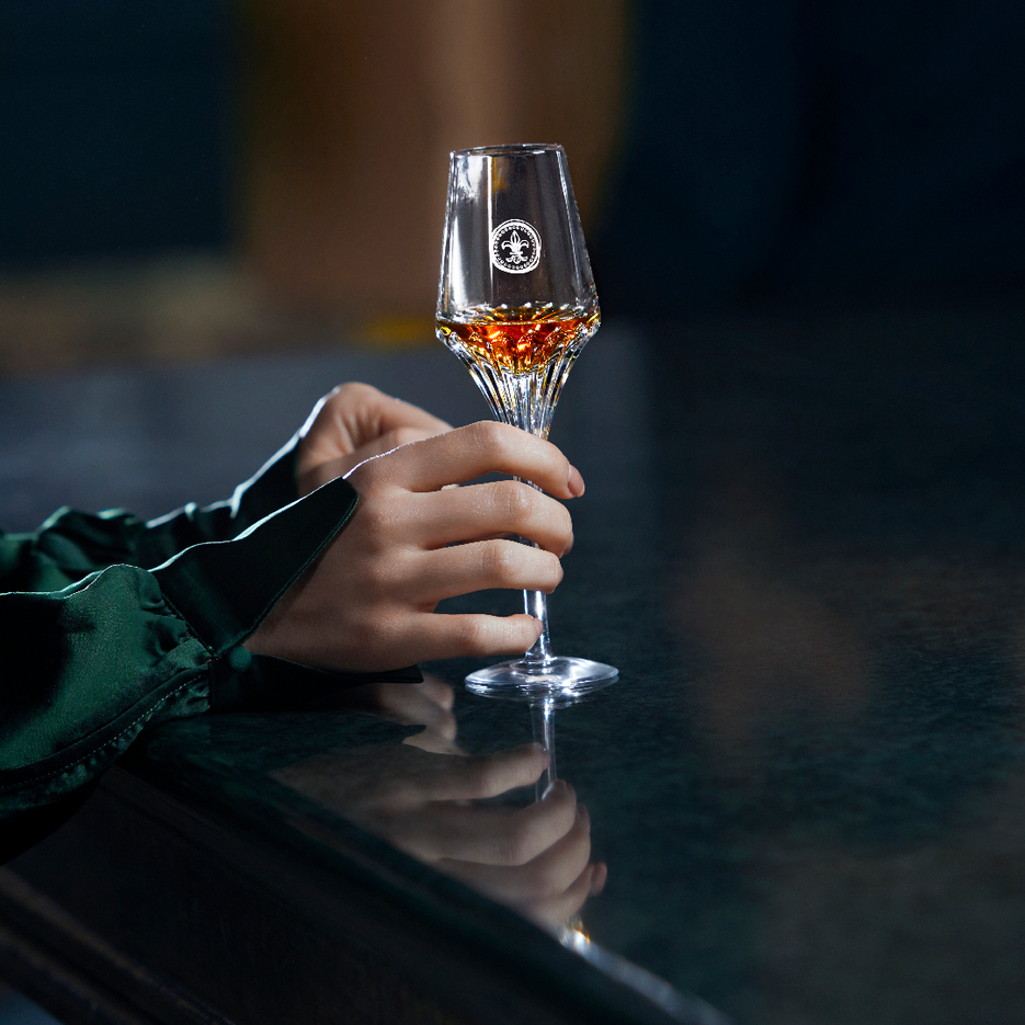 A lifestyle image of two female hands holding a crystal LOUIS XIII glass on the piano surface