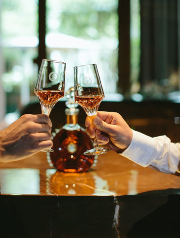 An image of two hands makong a toast with LOUIS XIII glasses, a decanter in the background