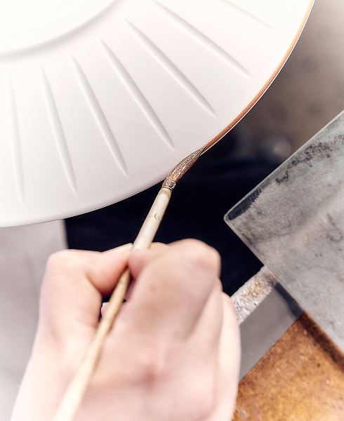  French artisan hand-painting the edge of a porcelain plate, highlighting french porcelain plates craftsmanship, porcelain manufactory tradition, quality dinnerware, unique patterns and alabaster white style from century French manufacturers.
