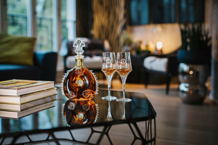 A lifestyle photo of LOUIS XIII decanter with two crystal glasses on a shiny surface, books nearby