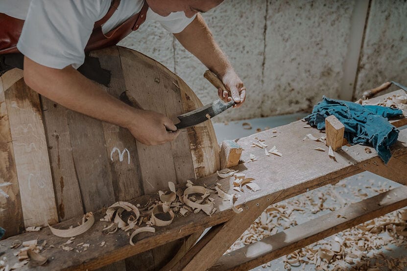 A photo of a manmaking a wooden barrel, scraps of wood around