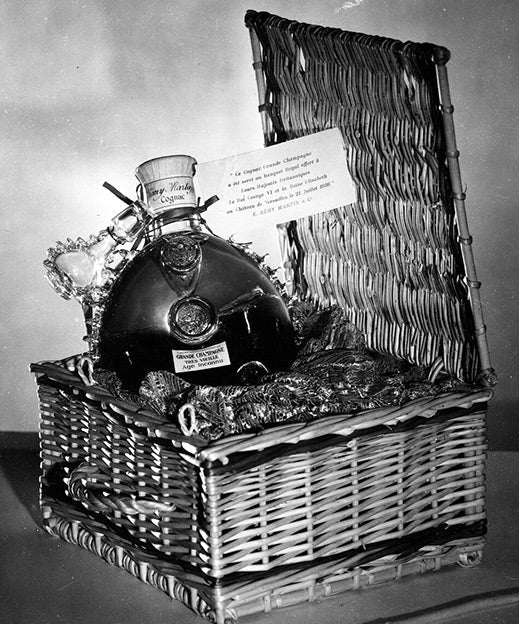 A black and white photo of a LOUIS XIII decanter in a willow basket