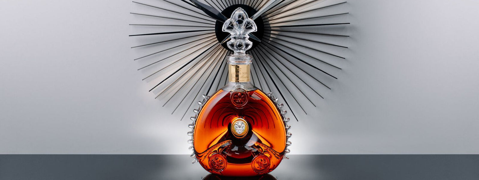 A lifestyle photo of LOUIS XIII decanter on a black surface with a black modent clock behind