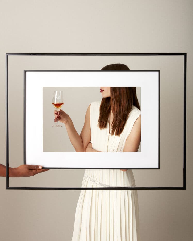 A lifestyle image of a woman holding LOUIS XIII crystal glass, in front a hand holding a picture frame