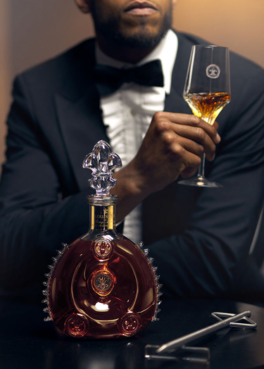 A photo of a man watching a bartender serving LOUIS XIII to a crystal glass