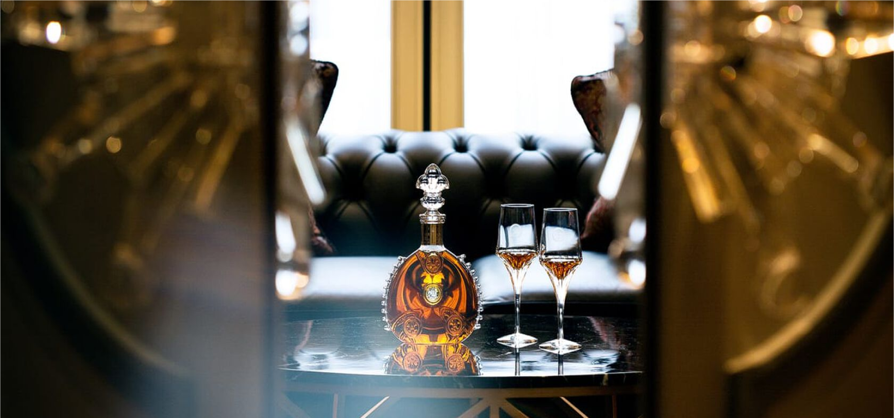 A lifestyle image of LOUIS XIII decanter with two crystal glasses seen through an open door