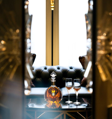 A lifestyle image of LOUIS XIII decanter with two crystal glasses seen through an open door
