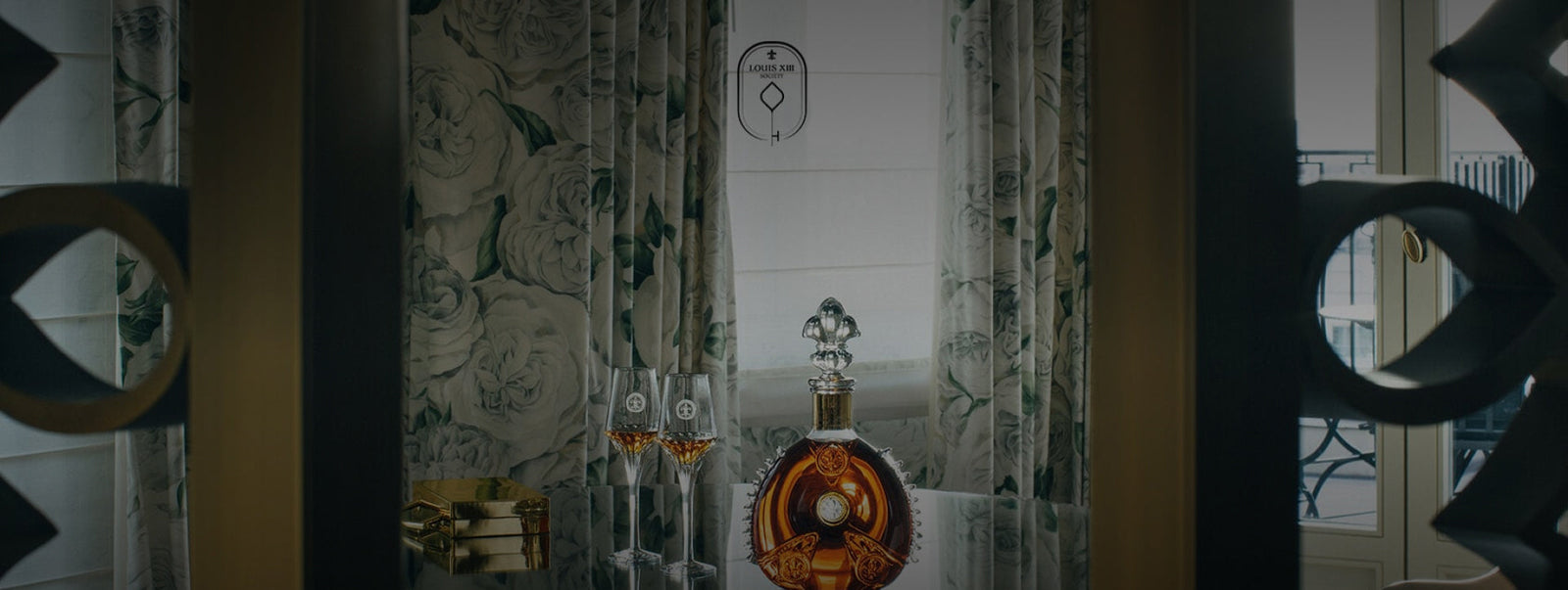 A dimmed lifestyle photo of a LOUIS XIII decanter and two filled crystal glasses on a piano