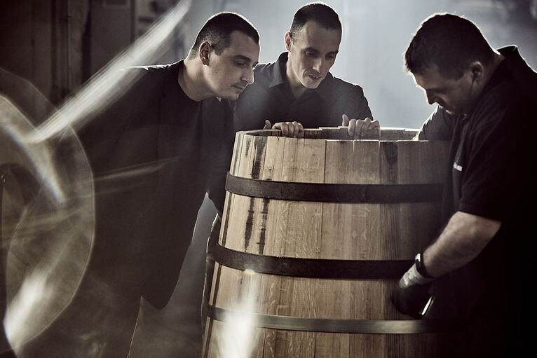 A photo of three people looking inside a big barrel